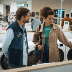 Deux personnes discutant devant une rangée de lave‑linge dans un magasin d’électroménager